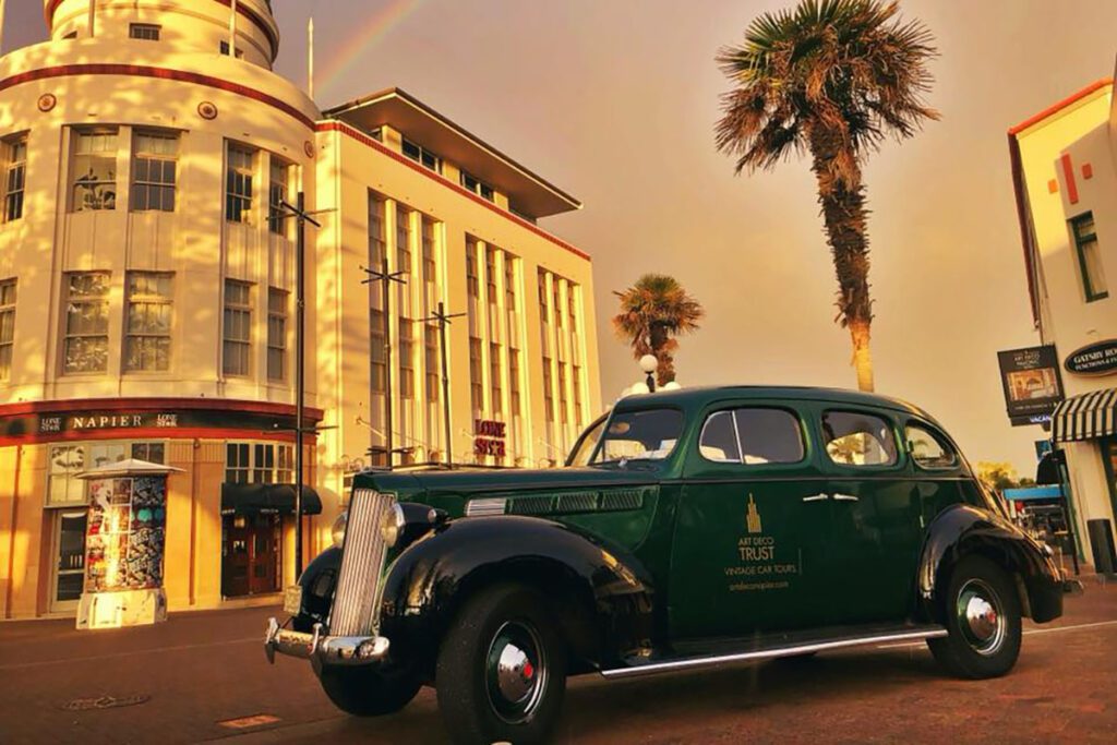 A green vintage car parked in front of an art deco building and a palm tree