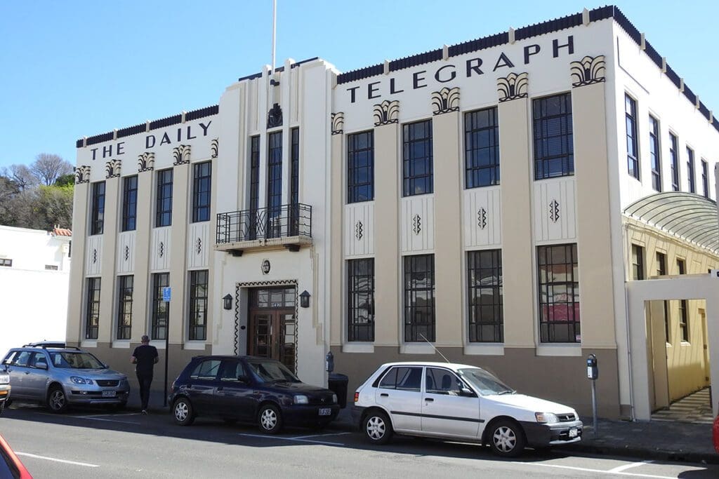 A cream and grey/blue art deco building with modern cars parked in front